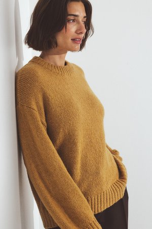Mosterdgele gebreide sweater met een ronde halslijn, geribde manchetten en onderrand. De stof lijkt zacht en textuurrijk, met een ontspannen pasvorm.
