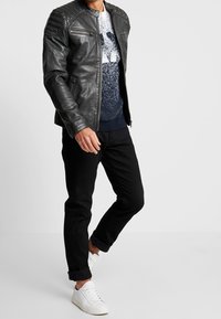 Svart läderjacka med räfflade axlar, med dragkedjeförsedda framfickor. Kombinerad med mörka jeans och vita sneakers, vilket ger en avslappnad stil.