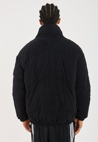 Veste doudoune en velours côtelé noir avec un col haut, une taille élastique et un motif matelassé au dos. Texture lisse et coupe décontractée.