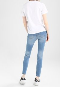 Jeans skinny de color azul claro con una textura suave, que presentan un diseño estándar de cinco bolsillos y delicados detalles de costura, llevados con una camiseta blanca.