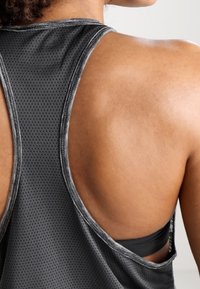 Canottiera atletica nera senza maniche con texture perforata, caratterizzata da una schiena bassa che rivela un reggiseno sportivo nero sottostante.