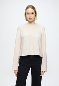 Sweat-shirt court rose pâle à manches longues et col rond. Texture douce, design simple, avec une petite étiquette sur le côté.