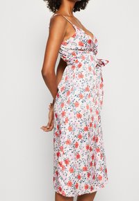 Robe fleurie avec un fond rose orné de fleurs rouges et bleues, corsage ajusté, fines bretelles, détail de ceinture à la taille, s'évasant jusqu'au midi.