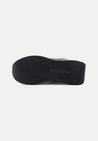 Semelle de sneaker en caoutchouc noir avec un motif de bande de roulement ondulé et une surface texturée. Présente le nom de la marque en relief au centre de la semelle.