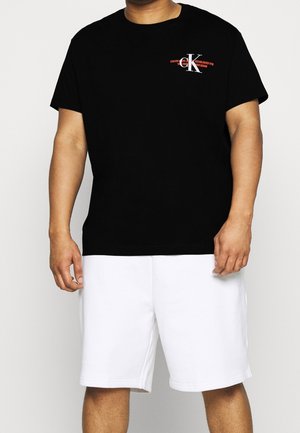 Czarna bawełniana koszulka z okrągłym dekoltem, ozdobiona małym białym i czerwonym logo na piersi; zestawiona z białymi bawełnianymi szortami.