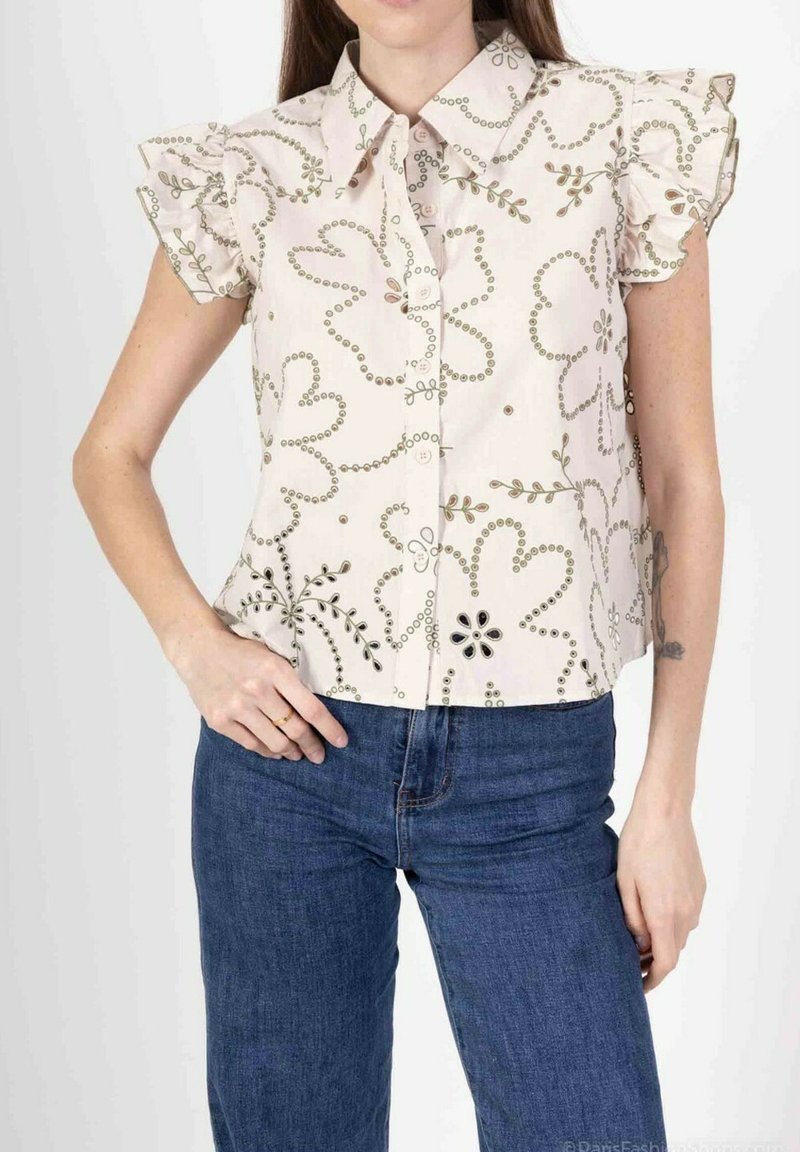 Blouse à manches courtes, de couleur claire, avec broderies florales et manches à volants ; elle possède un devant boutonné et un col rond.
