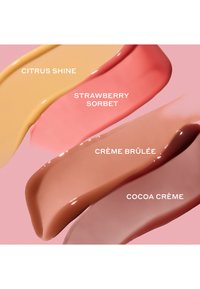 Cuatro muestras de tonos de labios cremosos: Citrus Shine (amarillo), Strawberry Sorbet (rosa), Crème Brûlée (nude), Cocoa Crème (marrón) sobre un fondo rosa.