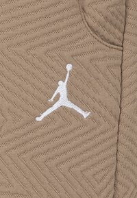 Kaki sporttyg med ett strukturerat zigzag-mönster och en vit broderad Jumpman-logotyp på vänster sida.