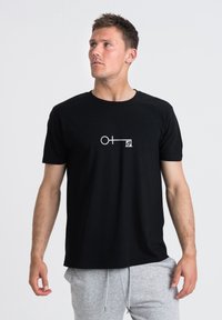 Svart bomullströja med korta ärmar som har en vit grafisk design av en cirkel och linje. Rund hals, avslappnad passform, slät textur.