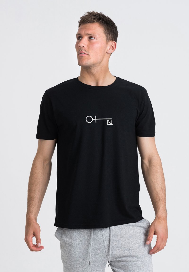 Svart bomullströja med korta ärmar som har en vit grafisk design av en cirkel och linje. Rund hals, avslappnad passform, slät textur.