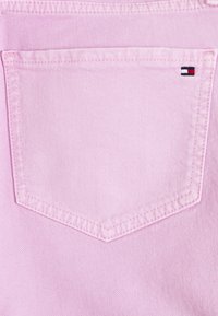 Pantalones vaqueros de mezclilla rosa claro con un diseño de sobrecostura en el bolsillo trasero y un pequeño logotipo bordado en rojo, blanco y azul en el borde del bolsillo.