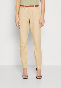 Beige chino's met een getailleerde pasvorm, voorzien van een riem en een gladde textuur. Gecombineerd met zwarte sandalen met bandjes.