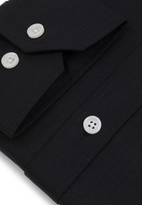 Czarna koszula z materiału z dwoma białymi guzikami. Posiada spiczasty kołnierz i strukturalne szwy. Widoczna faktura w tkani.