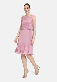 Różowa bezrękawnikowa sukienka z teksturowanym, haftowanym gorsetem i plisowanym dołem. Srebrne sandały na paski dopełniają całość.
