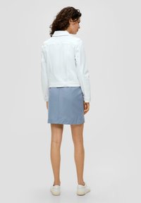 Witte denimjack met een kraag en lange mouwen, gecombineerd met een lichtblauwe rok en witte sneakers. Het jack heeft een cropped pasvorm en knoopdetails.