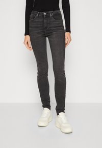 Jeans negros ajustados de denim con cintura alta, dos bolsillos frontales y costuras sutiles. Combinados con zapatillas blancas de plataforma.