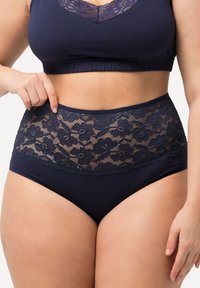 Reggiseno blu scuro e mutande a vita alta realizzati in tessuto morbido, con un bordo in pizzo floreale in vita e un bordo superiore liscio.