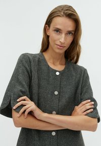 Rochie gri cu model espiga, mâneci scurte, decolteu rotund și nasturi argintii ca accente. Textură moale și croi structurat, potrivită pentru purtarea casual.