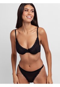 Black lingerie set featuring a scalloped lace trim on the bra and thong, made from soft, sheer fabric with adjustable straps.