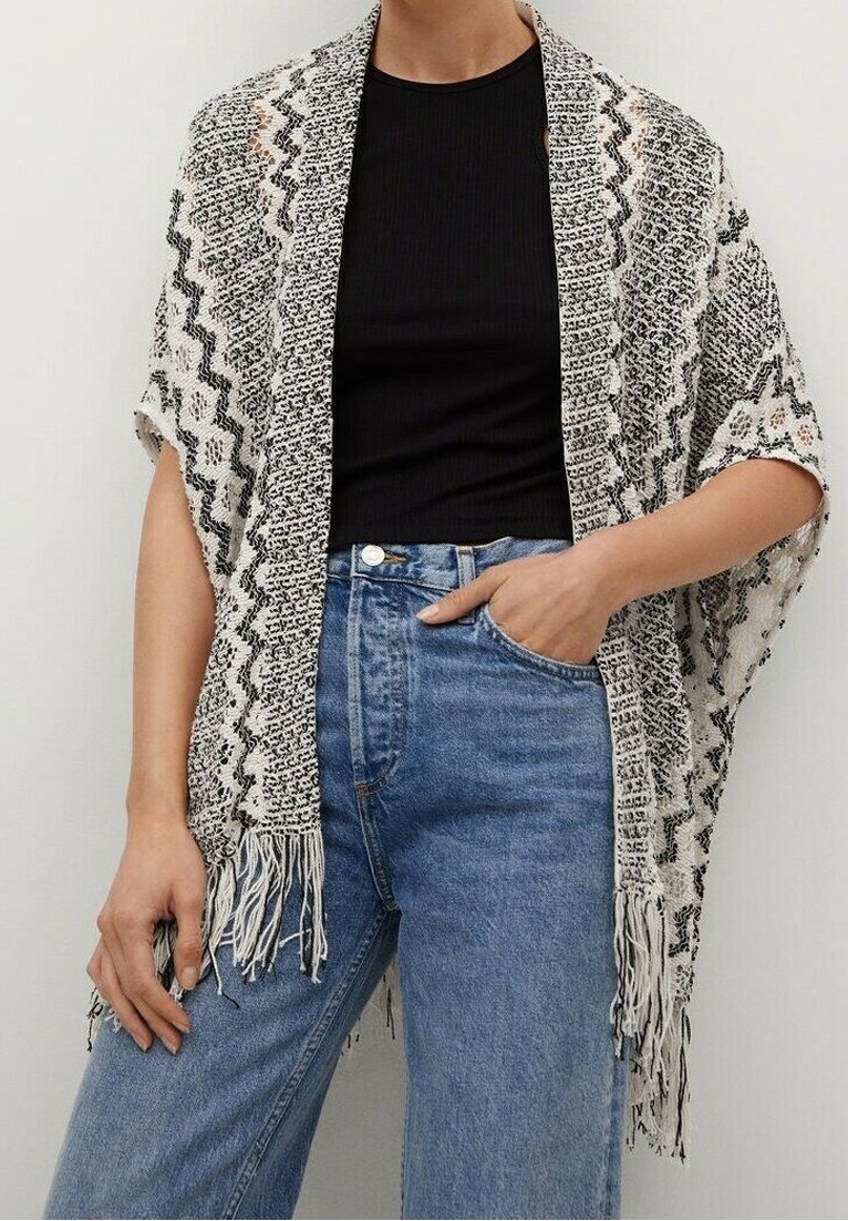 Lekki kimono z frędzlami w czarno-białym wzorze zygzaków, noszone na czarnej bluzce i niebieskich, wysokich dżinsach.