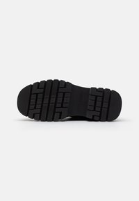 Black rubber shoe sole with deep tread patterns, featuring grooves and ridges for traction. Flat profile and no additional embellishments.