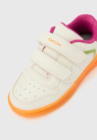 Balta sporta apavi ar divām Velcro siksnām, rozā un zaļiem akcentiem, perforētu tekstūru un oranžu gumijas zoli. Sānos redzams logotips "GEOX".