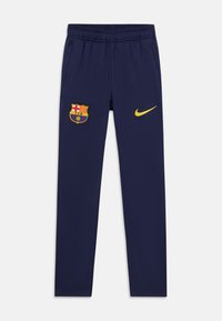Tumši zili sporta bikses ar elastīgu jostu, FC Barcelona emblēma kreisajā augšstilbā un dzeltenais Nike zvīņotājs labajā augšstilbā.