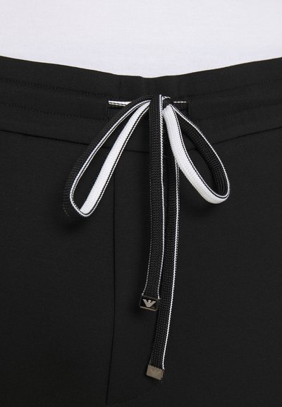 Zwarte joggers met een trekkoord in de taille, voorzien van contrasterende zwart-witte strepen en metalen accenten aan de uiteinden van de trekkoorden.
