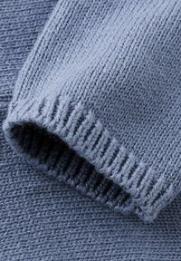 Niebieski dzianinowy sweter w zbliżeniu, ukazujący prążkowany mankiet oraz teksturowany korpus o miękkim, średniej wagi wyglądzie.