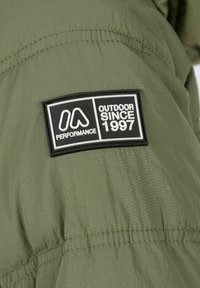 Zelena zunanja jakna z teksturiranim zaključkom. Značilna je črna nalepka z napisom "OUTDOOR SINCE 1997" in logotip blagovne znamke. Opazne detajle šivanja.