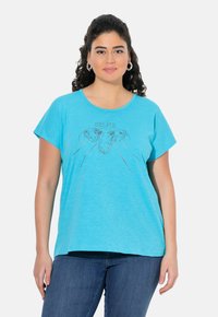 Camiseta de manga corta en color turquesa con un corte relajado, que presenta un diseño impreso de rostros de perros y la palabra "SELFIE" encima de ellos.