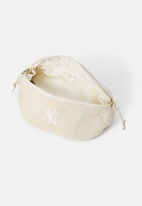Pochette en velours côtelé beige avec fermeture éclair blanche et logo blanc brodé des New York Yankees, partiellement ouverte montrant l'intérieur en tissu crème.