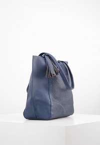 Námořnická kožená taška přes rameno s perforovaným vzorem, bočními třásněmi a strukturovaným tvarem. Povrch je hladký s matným povrchem.