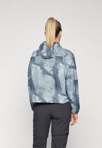 Leichte, kurz geschnittene blaue Jacke mit einem strukturierten, marmorierten Muster und Kapuze. Verfügt über eine Markierung auf der Rückseite in der Nähe des Saums und der Bündchen.