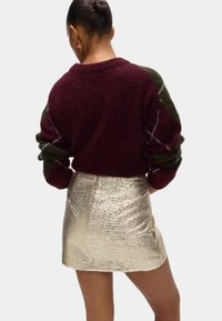 Suéter de gran tamaño en burdeos y verde con tejido texturizado, combinado con una falda mini metálica dorada que presenta un patrón arrugado.