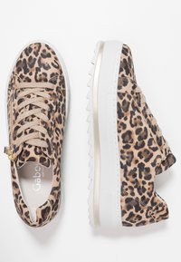 Des baskets imprimées léopard présentent un tissu texturé, une base beige, des accents dorés et une semelle en caoutchouc blanche avec un motif en zigzag.