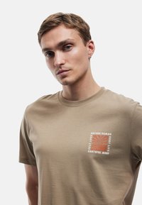 Khaki bawełnina t-shirt z okrągłym dekoltem, z nadrukiem graficznym w kolorze białym i koralowym, zawierającym motywacyjne hasła oraz wzór słońca.