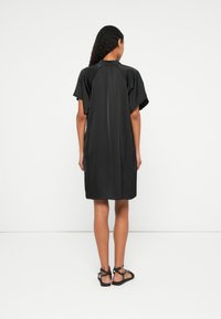 Vestido preto de manga curta com um corte solto, apresentando um decote redondo e uma textura suave. Usado com sandálias pretas com tiras.