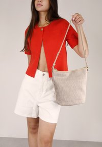 Cárdigan de punto rojo de manga corta con un botón en el frente y un bolso de bucket de textura beige con correa de hombro, combinado con pantalones cortos blancos.