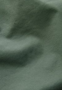 Gros plan d'un tissu vert olive lisse avec une fine texture côtelée diagonale et des plis doux créant des ombres subtiles.
