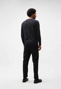 Dark gray sweater with a textured knit, round neckline, and long sleeves, paired with black trousers and boots, viewed from the back.