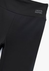 Czarne legginsy sportowe o gładkiej, elastycznej fakturze. Posiadają wysoki stan oraz nadrukowany tekst "TWÓRZ. INSPIRUJ." na pasku.