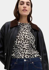 Svart läderjacka med en brun manchesterkrage, bärs över en vit och svart leopardmönstrad topp, matchad med mörkblå jeans.