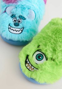Blaue und grüne flauschige Hausschuhe mit Cartoon-Monster-Gesichtern, die gestickte Augen, Zähne und lächelnde Münder auf einem weißen Hintergrund zeigen.