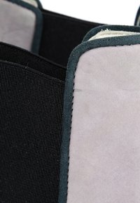 Gros plan d’un tissu gris clair avec un bord vert foncé et une large bande élastique noire attachée.