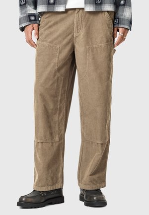 Pantalon en velours côtelé marron avec une coupe décontractée, doté de poches plaquées, d'une texture à rainures subtile et de jambes droites. Porté avec des chaussures noires.