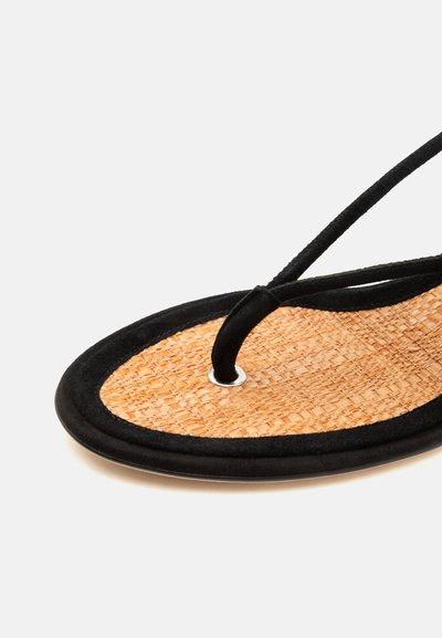 Gros plan sur une sandale avec une semelle en paille tissée et un entre-doigt ainsi que des brides en daim noir.