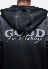 Haut à capuche noir avec un design dégradé. Présente un grand texte "GOOD" et "For Nothing" écrit à la main au dos. Tissu doux et style à capuche.