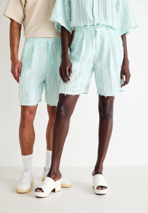 To personer iført lyseblå teksturerte shorts; den ene kombinerer dem med hvite joggesko og sokker, mens den andre har på seg hvite hæle sandaler.