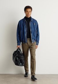 Modra jeans jakna, črna roll neck majica, bež hlače, črni čevlji, nosi črno usnjeno torbo. Gladke teksture, sproščen kroj.